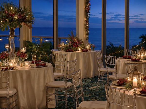 Holiday-decorated event tables with candlelight and red floral centerpieces overlooking the ocean at Ocean Grand ballroom, Sole Miami resort in Sunny Isles Beach